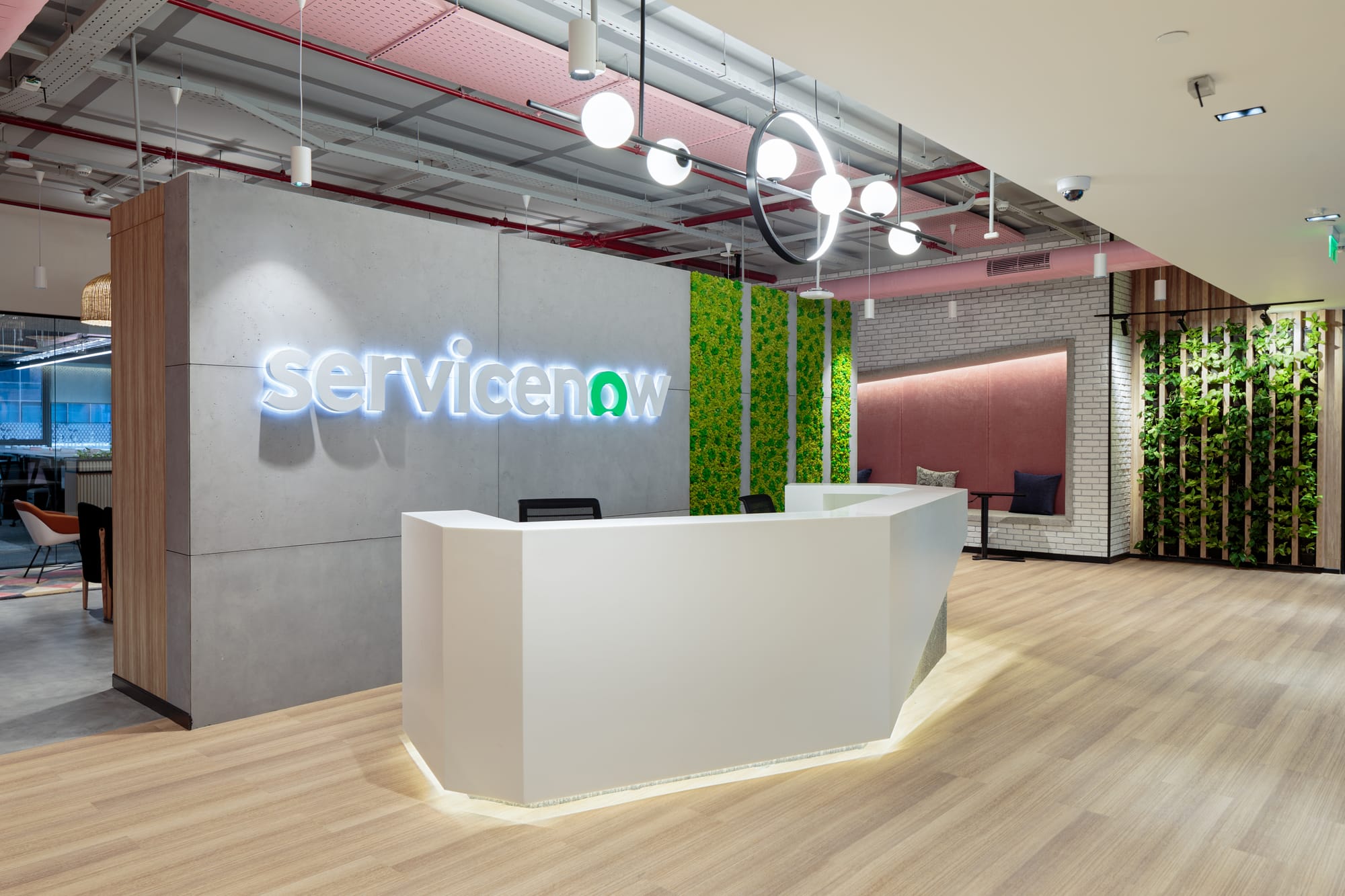 ServiceNow office lobby with a white reception desk, illuminated logo, wood floors, and green plant walls.