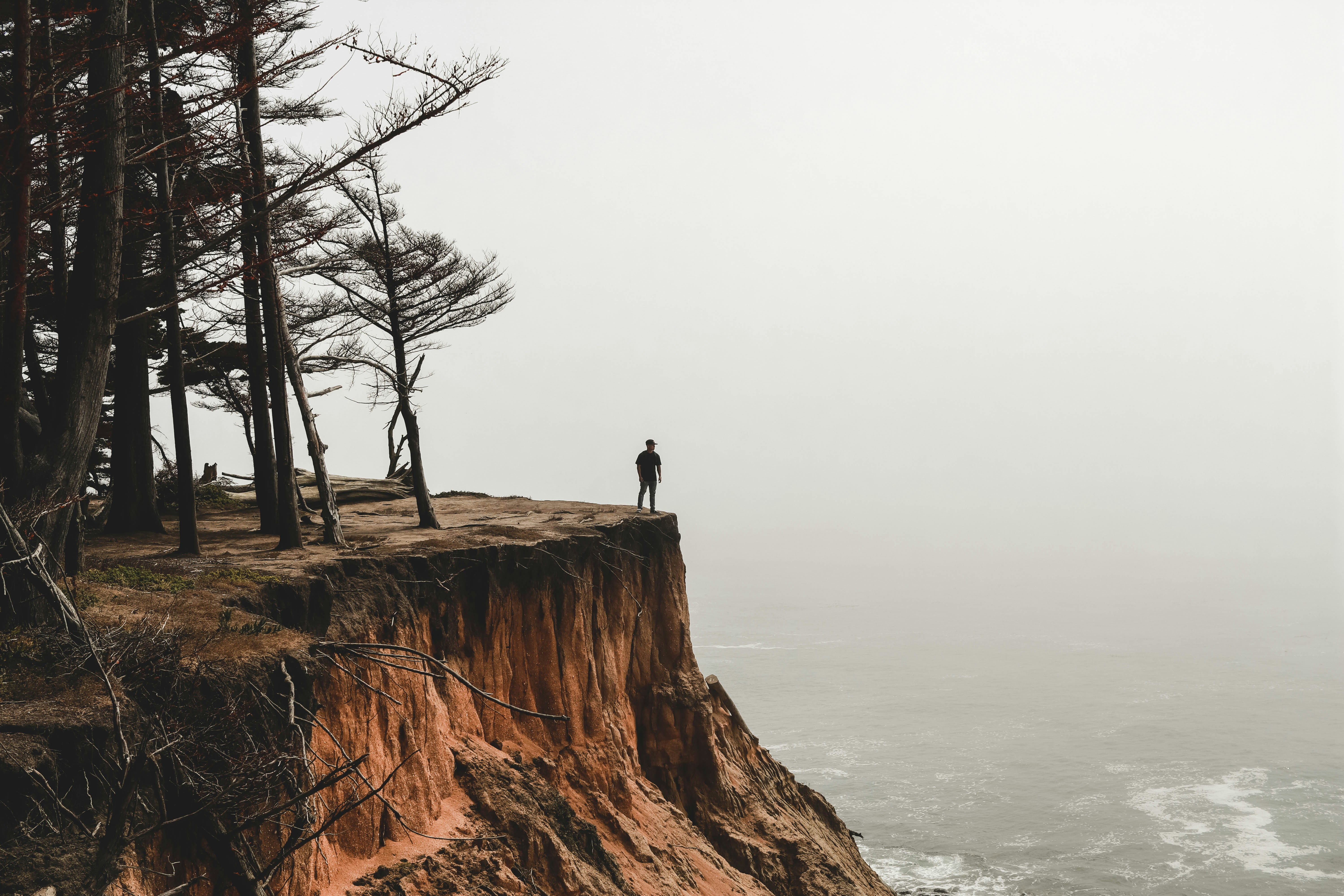 Man standing at edge of a cliff overlooking a misty ocean.