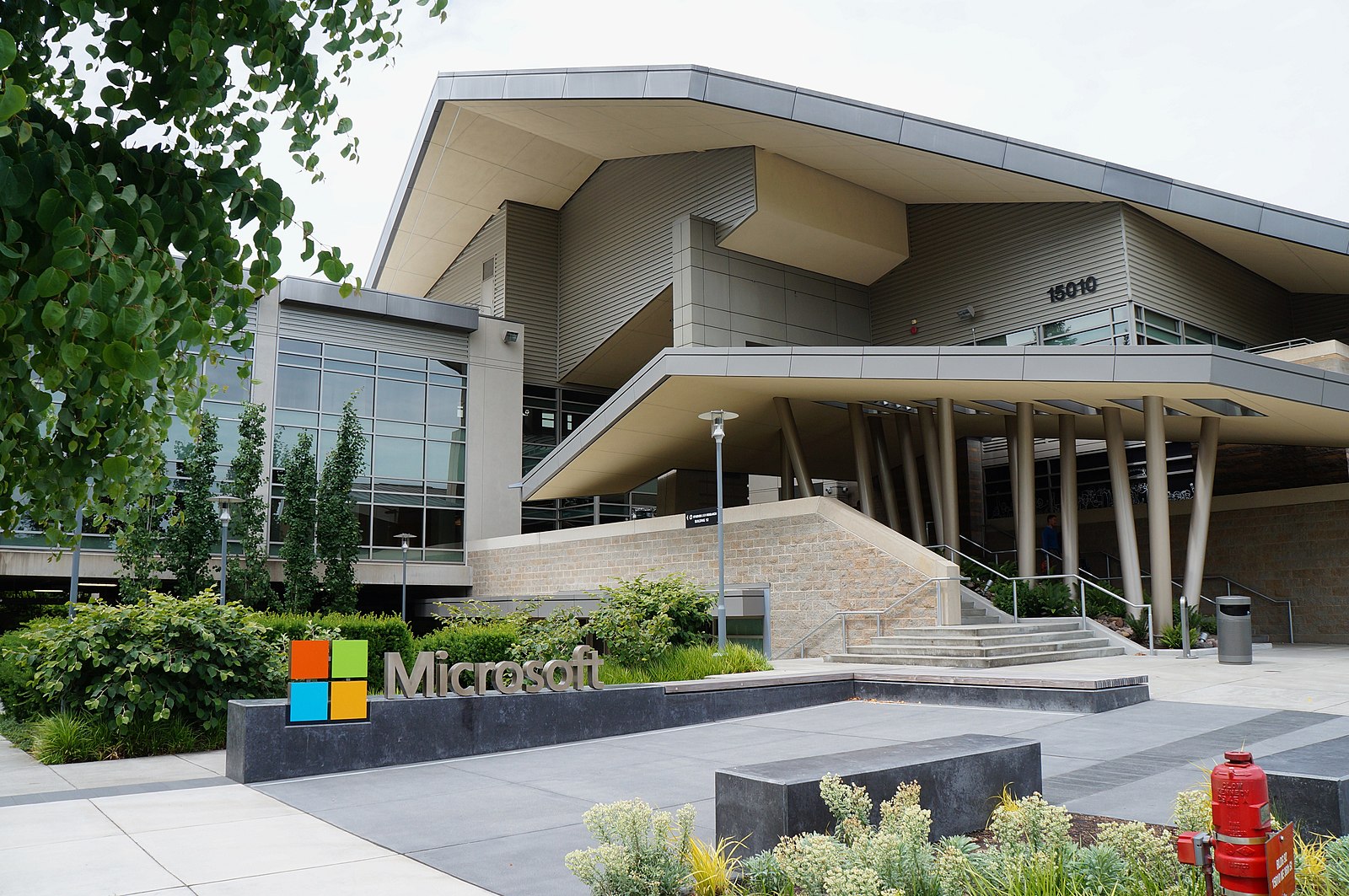 Exterior view of Microsoft’s Redmond campus, showing a modern building with large windows, angled rooflines, landscaped greenery, and a prominent Microsoft logo sign in front.