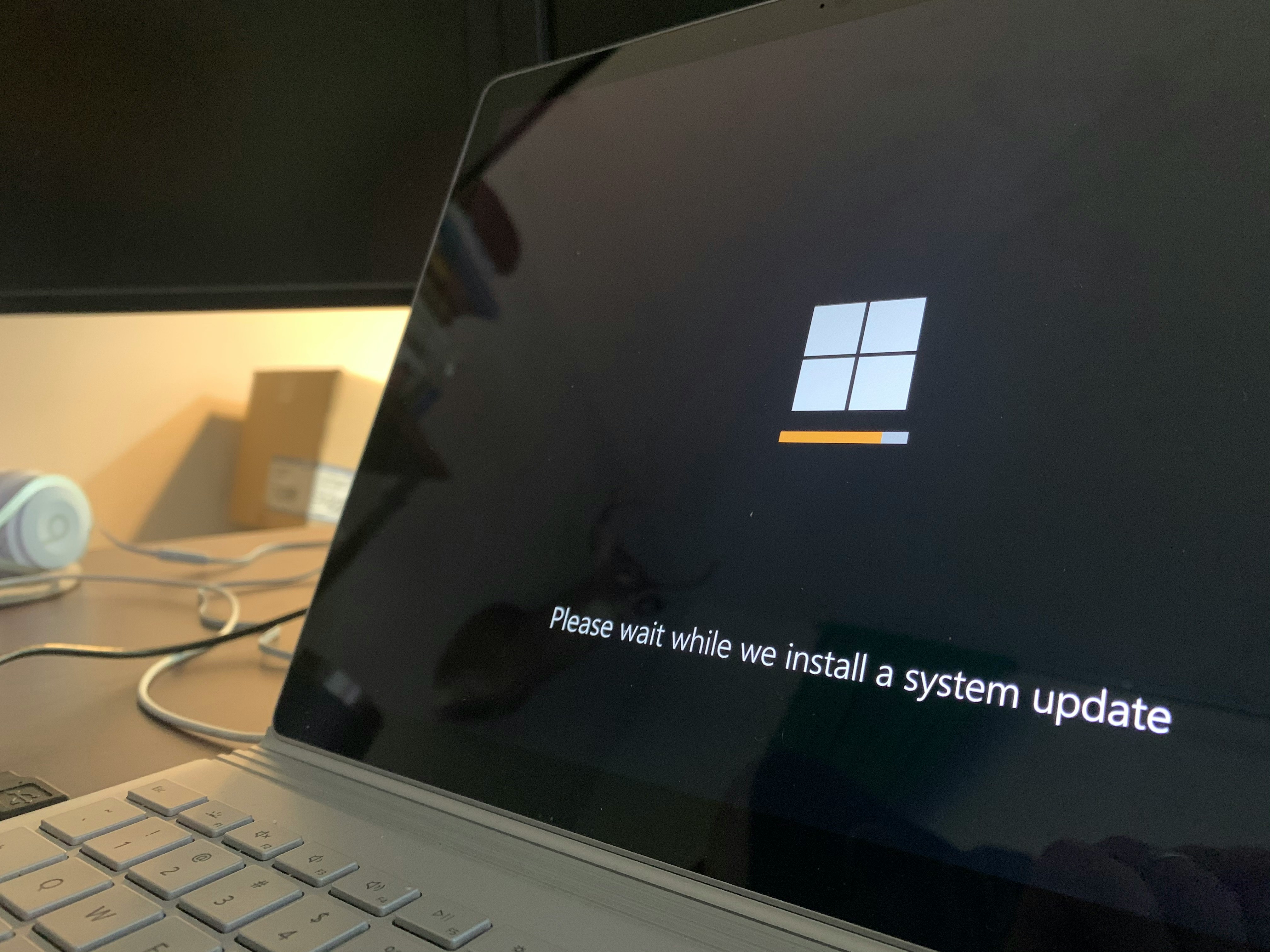 Close-up of a laptop screen showing a Windows system update in progress with the message “Please wait while we install a system update.”