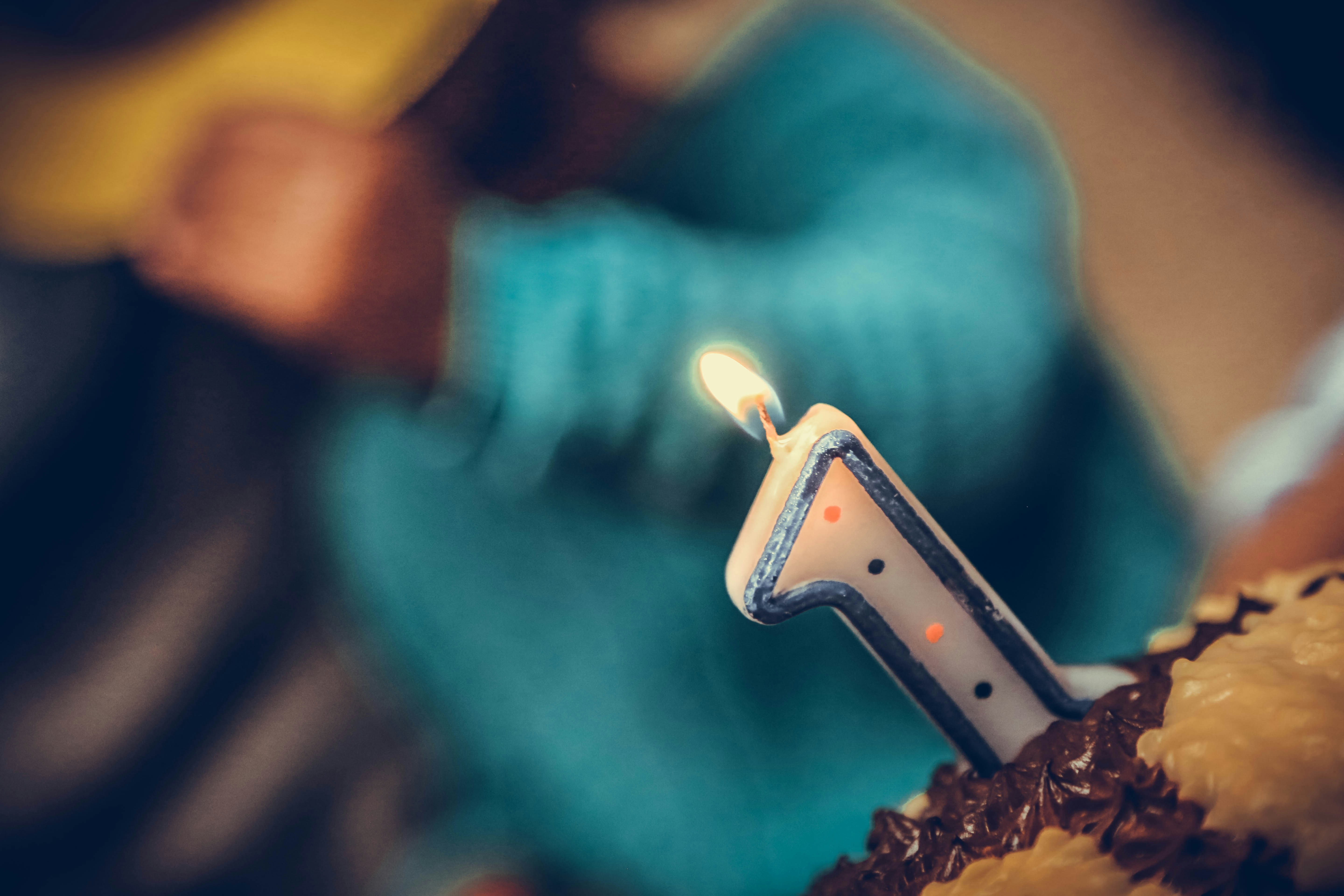 Close-up of a lit birthday candle shaped like the number one, placed on a frosted cake with chocolate and yellow icing.