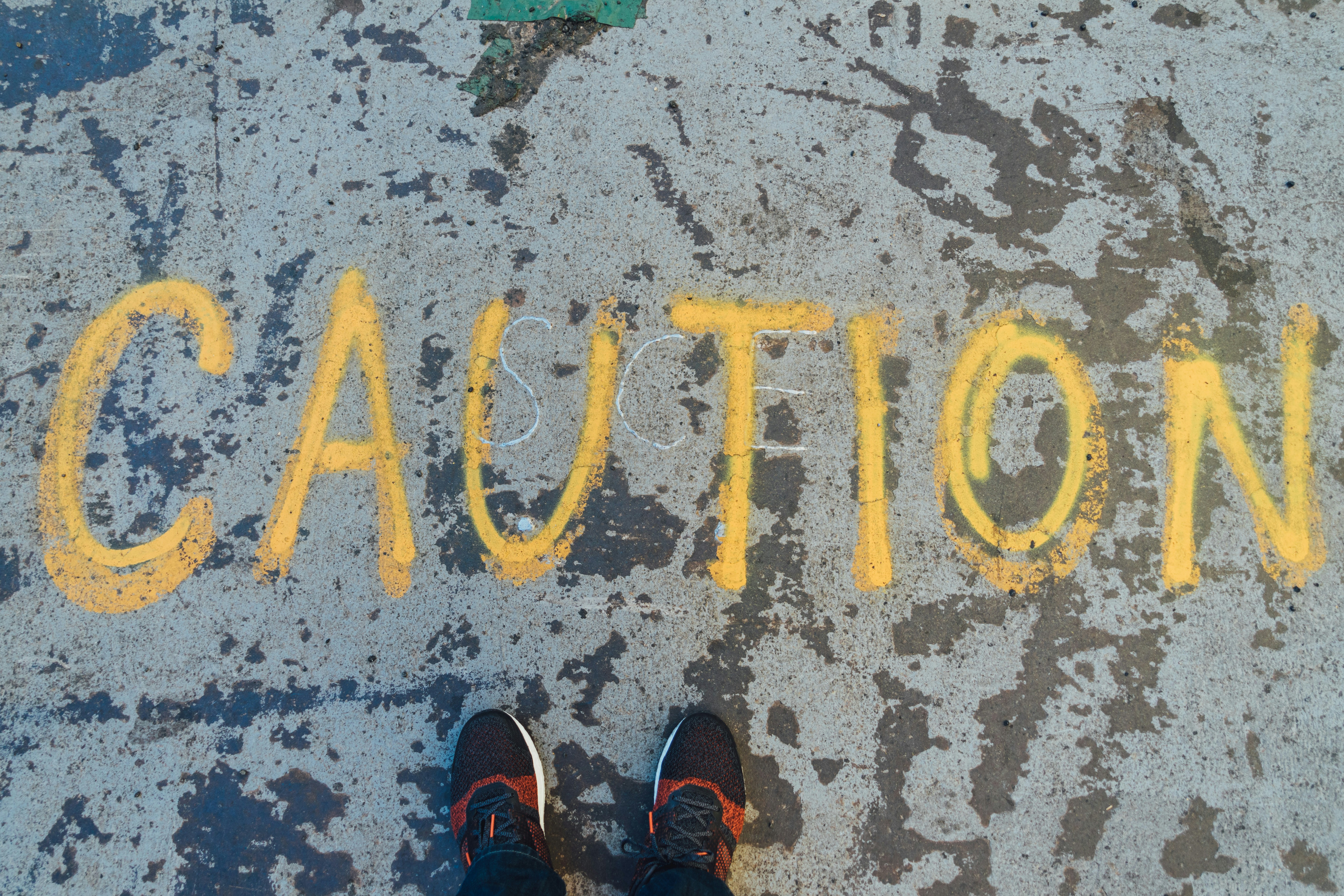 The word caution painted in yellow in all caps against a gritty looking concrete wall.