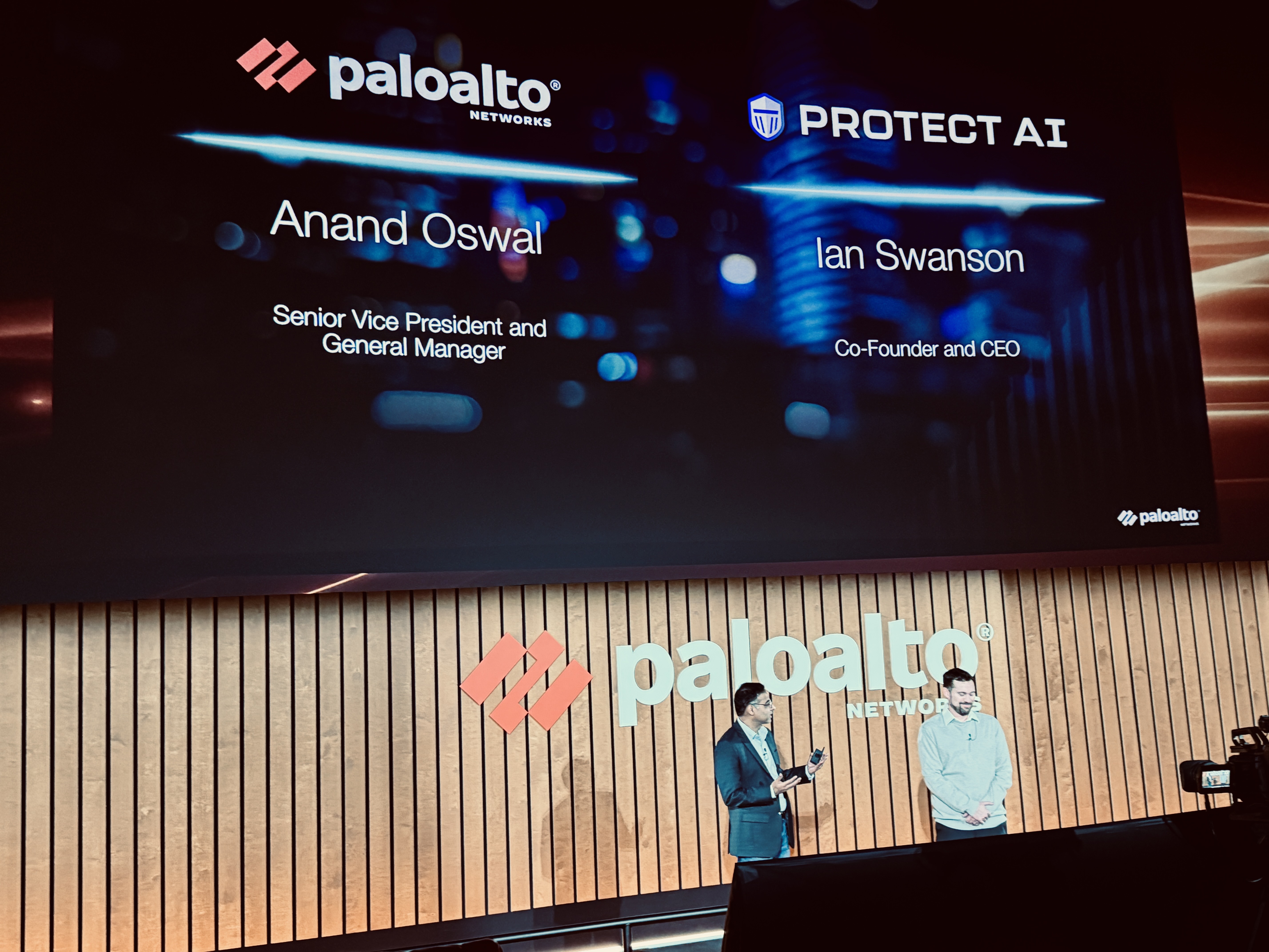 Palo Alto Networks senior vice president and general manager Anand Oswall and Protect AI co-founder and CEO Ian Swanson on stage together with Slide over their heads with their names.