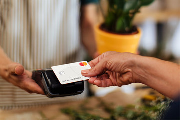 Hand reaching out with white Mastercard touching a card reader.