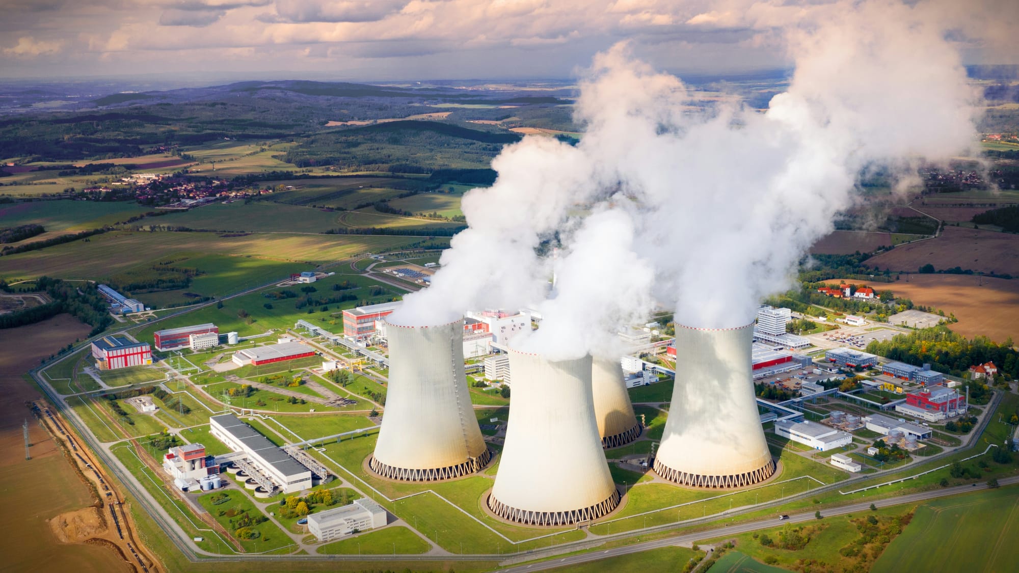Aerial view of a nuclear power plant with large cooling towers releasing steam into the sky.