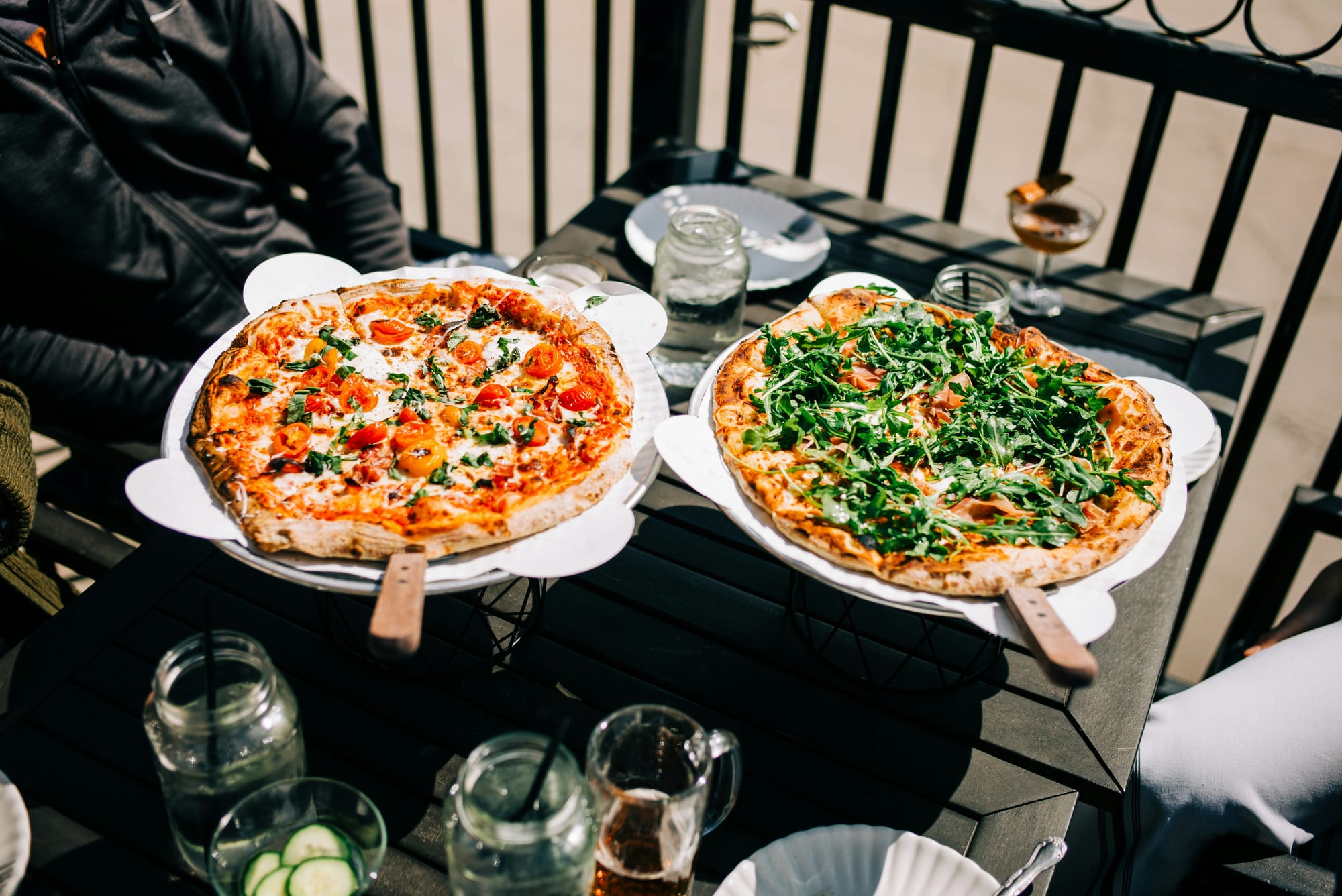 Two pizzas being served on a small outdoor table.