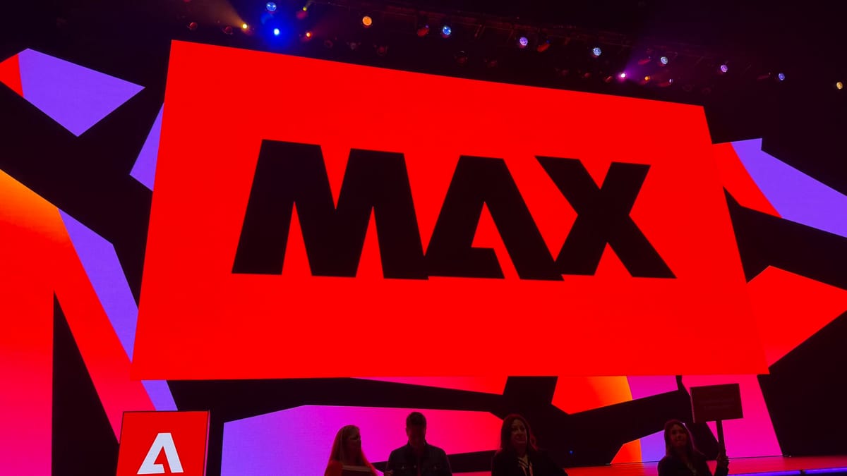 Stage at Adobe Max 2025 featuring a large red screen with the word “MAX” in bold black letters, illuminated by colorful light