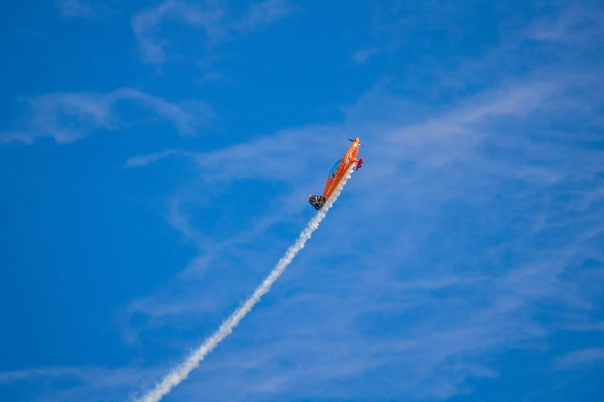 A small red airplane flying through a blue sky