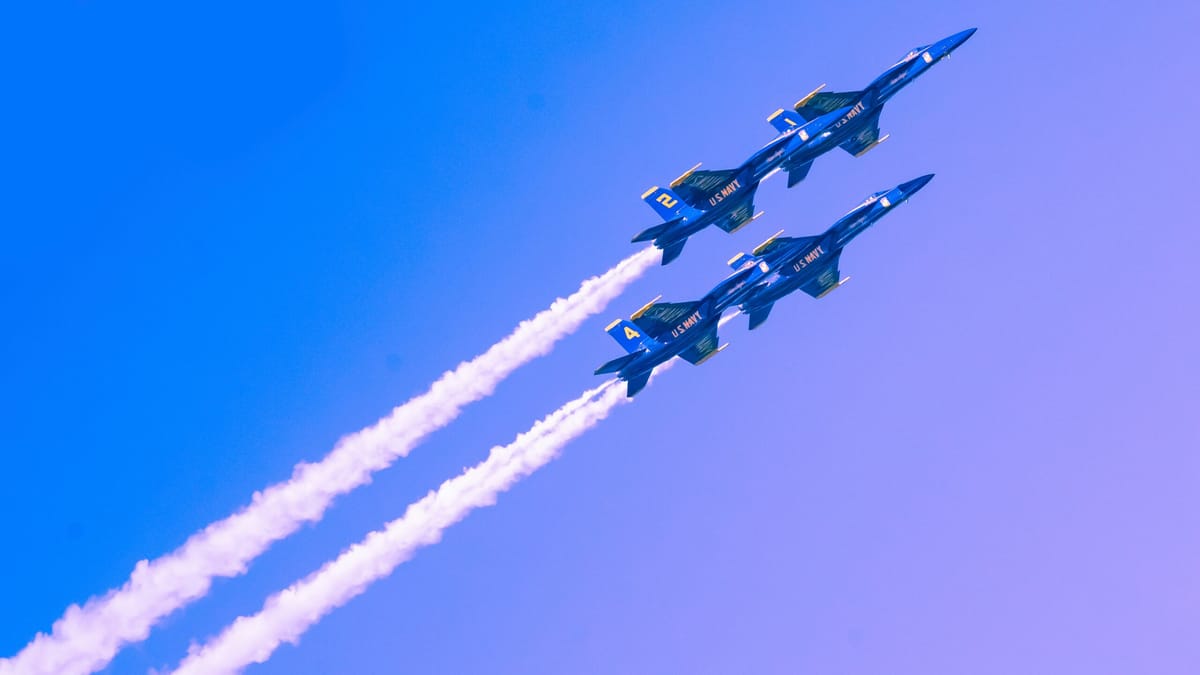 Four U.S. Navy Blue Angels fighter jets flying in tight formation against a clear blue sky, leaving white vapor trails.