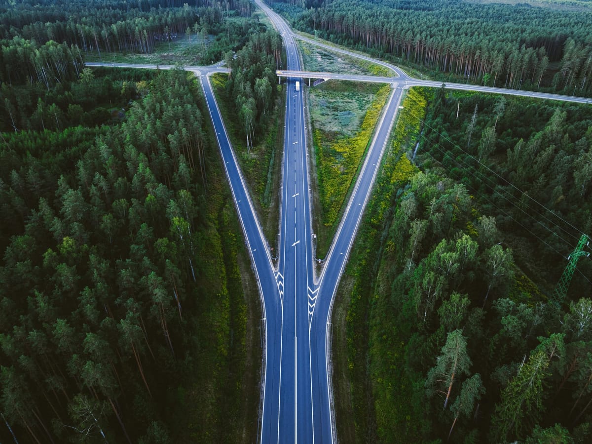 Aerial view of a highway splitting into two directions through a dense green forest, symbolizing a crossroads or decision poi