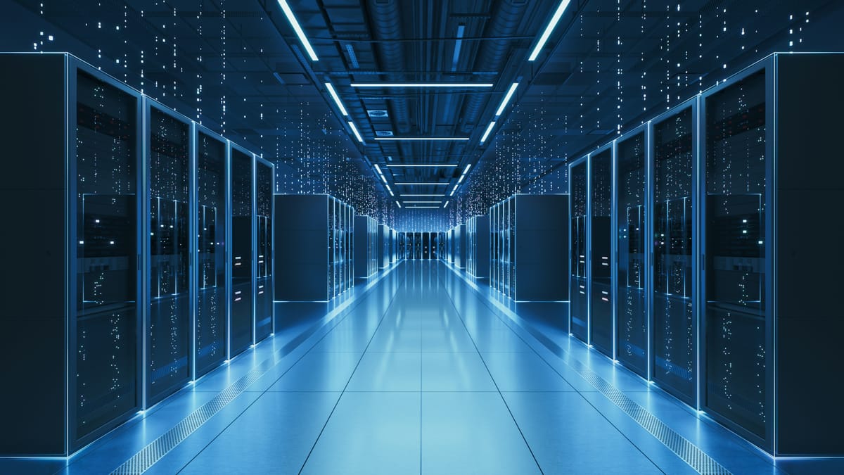Rows of illuminated server racks inside a modern data center, blue LED lighting reflecting off a polished floor with overhead cables and conduits visible along the ceiling.