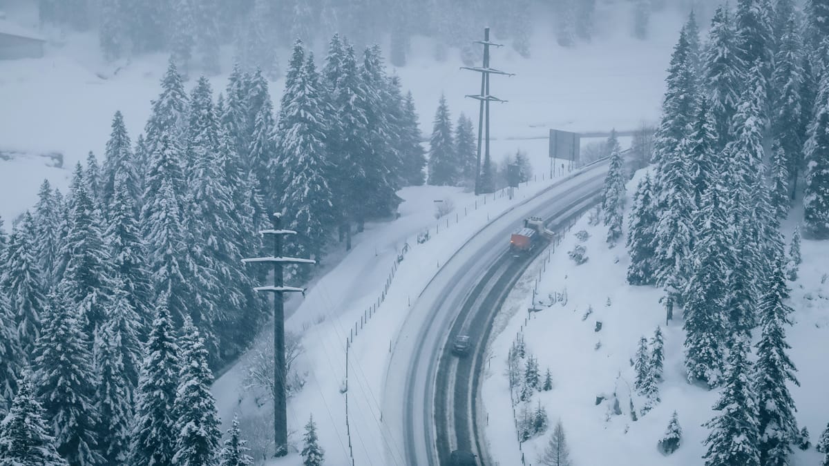 Plow clearing a snowy road in the middle of a storm.
