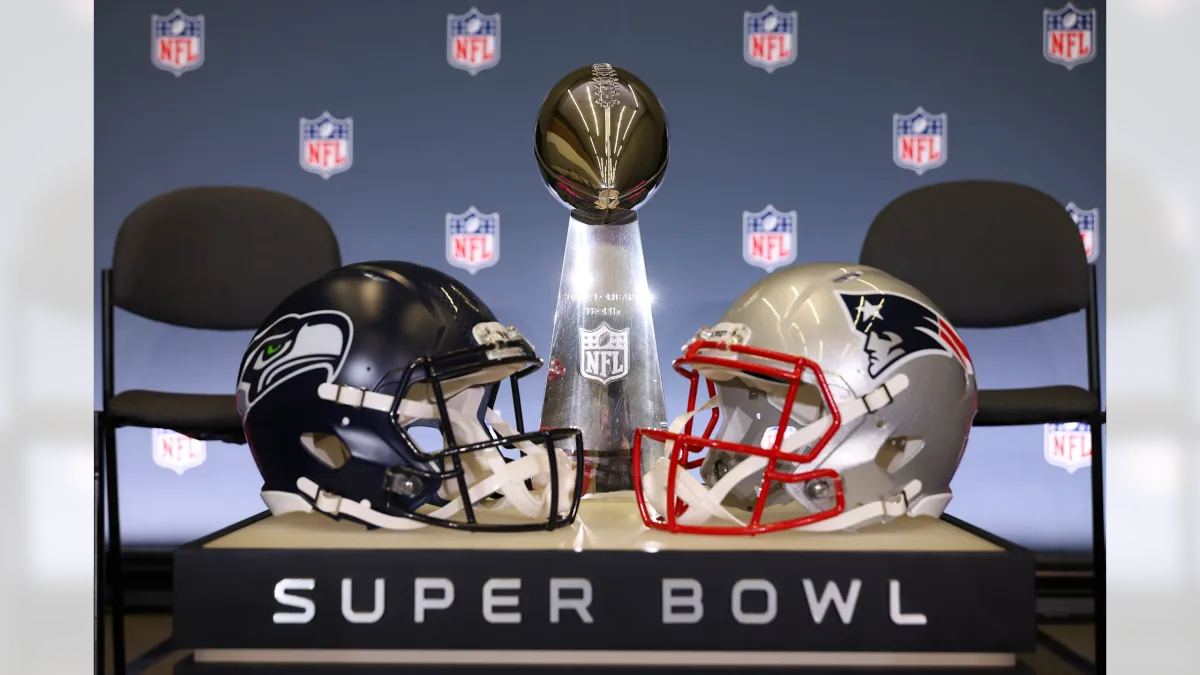 The Vince Lombardi Trophy positioned between football helmets from the Seattle Seahawks and New England Patriots at a Super Bowl event.