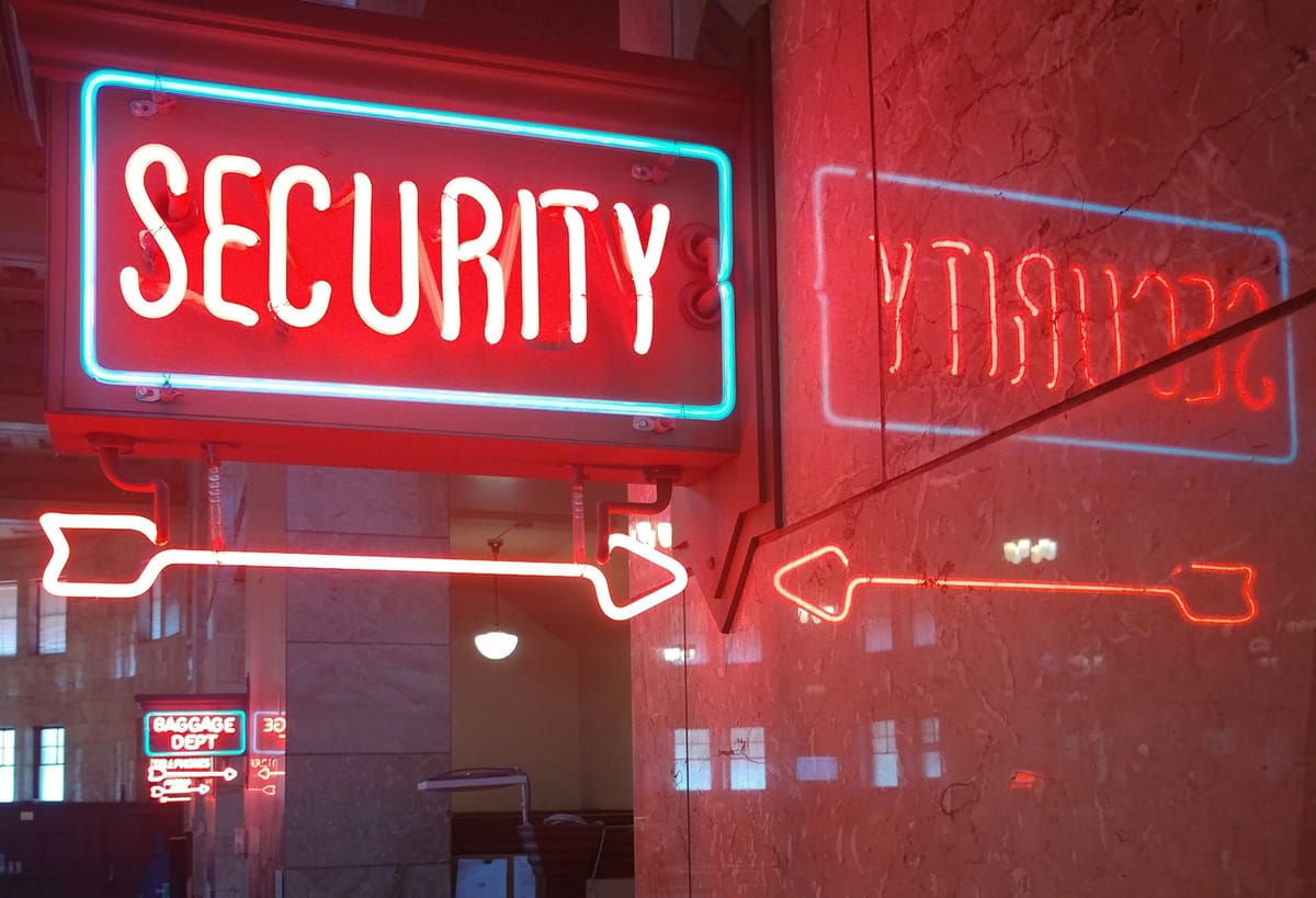 Neon “Security” sign with arrow, reflected in a glass wall inside a building interior.