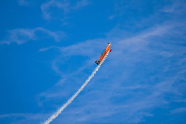 A small red airplane flying through a blue sky