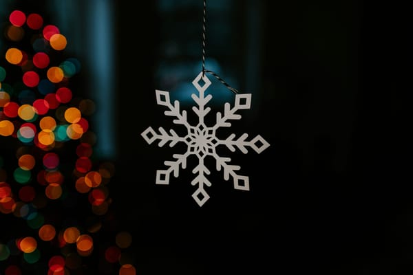Gold metal snowflake hanging from string with colors in backgrond.