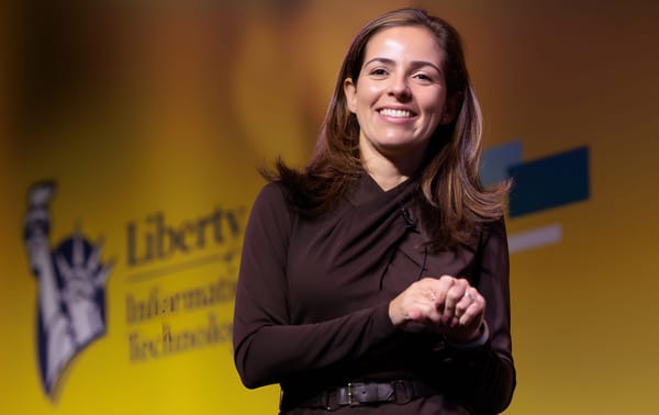 Monica Caldas, global CIO at Liberty Mutual Insurance Company smiling in front of the Liberty Mutual logo.