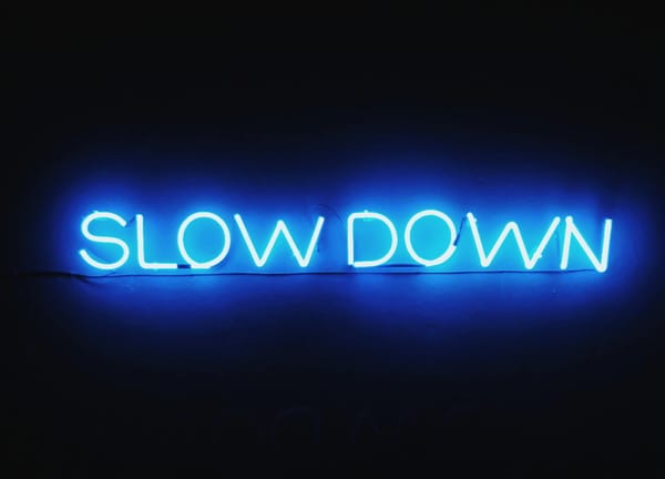 Blue neon sign on a dark background displaying the words “SLOW DOWN.”