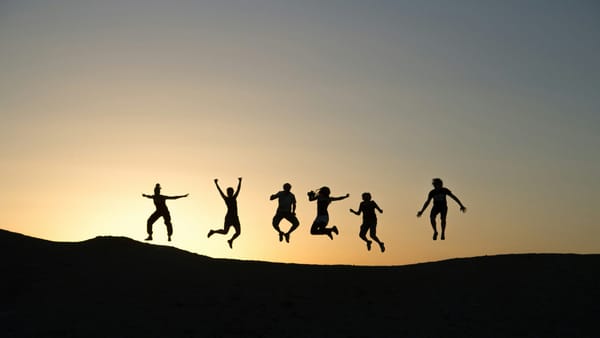 Silouetted group people leaping in the air against a sunset backdrop.