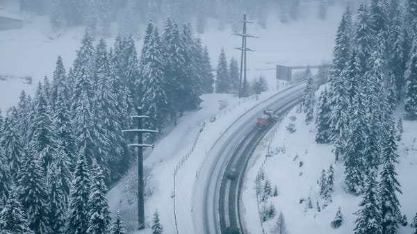 Plow clearing a snowy road in the middle of a storm.