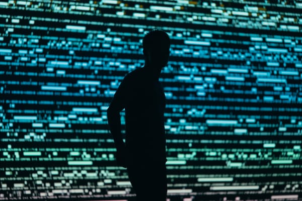 Silhouette of a person standing before a large wall of glowing digital data streams.